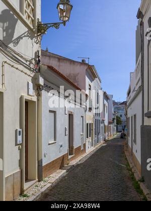 Gebäude auf einer schmalen Kopfsteinpflasterstraße in der Stadt Lagos in der Region der Algarve im Süden Portugals, bekannt für ihre ummauerte Altstadt, Klippen und den Atlantik Stockfoto