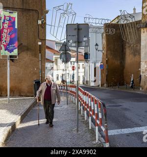 Älterer Mann, der mit einem Stock auf einem Bürgersteig in der Stadt Lagos in der südportugiesischen Algarve spaziert, die für ihre ummauerte Altstadt, Klippen und bekannt ist Stockfoto