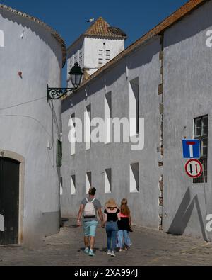 Rückansicht der Touristen, die durch eine enge Gasse in Faro, der Hauptstadt der südportugiesischen Algarve, spazieren. Der neoklassizistische Bogen der Stadt Stockfoto