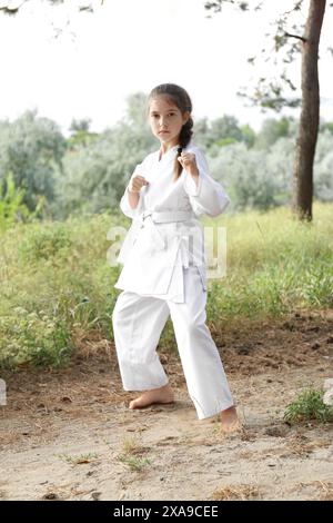 Süßes kleines Mädchen im Kimono, das draußen Karate übt Stockfoto