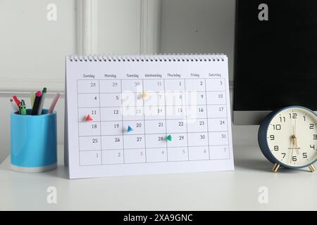 Zeitplan. Kalender mit gekennzeichneten Daten, Wecker und Schreibwaren auf weißem Tisch drinnen Stockfoto