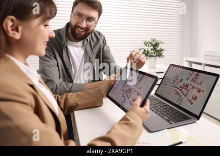 Kartografen arbeiten mit Katasterkarten auf Tablets am weißen Tisch im Büro Stockfoto