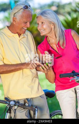 Glückliche Seniorinnen und Seniorinnen verbinden sich mit dem Fahrrad in einem Park mit hellblauem Himmel mit einer App auf einem Handy Stockfoto