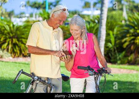 Glückliche Seniorinnen und Seniorinnen verbinden sich mit dem Fahrrad in einem Park mit hellblauem Himmel mit einer App auf einem Handy Stockfoto