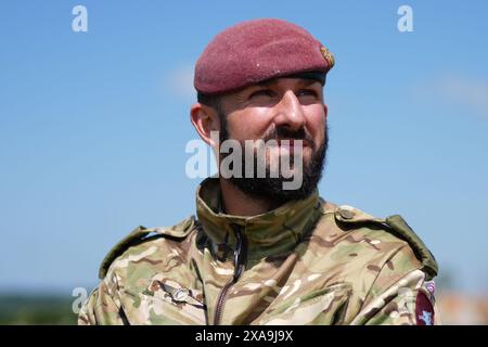 Captain Maik Biggs vom 16. Medizinischen Regiment, dessen Großvater im Zweiten Weltkrieg für die Nazis kämpfte, posiert, nachdem er an einem Fallschirmsprung an der Seite der britischen, belgischen, kanadischen und US-Streitkräfte teilgenommen hatte. organisiert von der Royal Air Force und der British Army über der 'Drop Zone K' in der Nähe von Sannerville, Frankreich, um die Rolle der Luftwaffe während der Landungen in der Normandie vor dem 80. Jahrestag des D-Day. Bilddatum: Mittwoch, 5. Juni 2024. Stockfoto