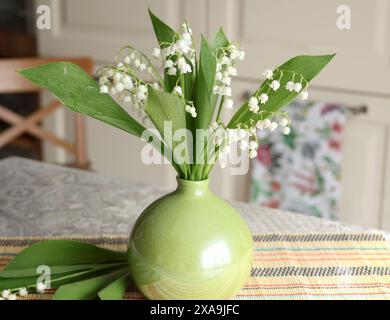 Blumenstrauß von Maiglöckchen in grüner Vase drinnen auf dem Tisch Stockfoto
