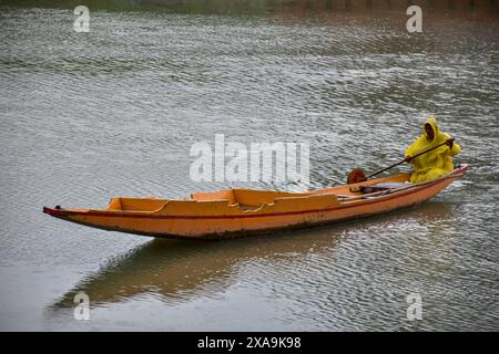 Ein Mann im Regenmantel reißt sein Boot über den Fluss Jehlum während des Regenfalls in Srinagar, der Sommerhauptstadt von Jammu und Kaschmir. Stockfoto