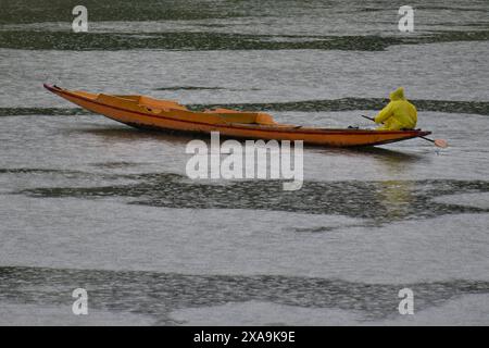 Ein Mann im Regenmantel reißt sein Boot über den Fluss Jehlum während des Regenfalls in Srinagar, der Sommerhauptstadt von Jammu und Kaschmir. Stockfoto