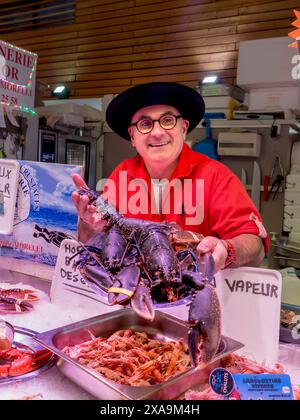 BLUE HUMSTER MARKET STAND CONCARNEAU FRANCE BRITTANY Concarneau im Inneren der französischen Fischmarkthalle und des Charakters Fischhändler im bretonischen Stil, der stolz seinen lokalen Live-blauen Hummer zum Verkauf zeigt Brittany Finistere France Stockfoto