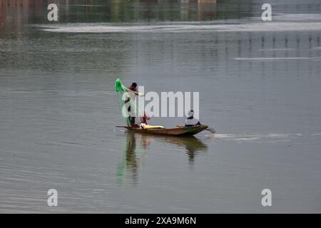 Srinagar, Indien. Juni 2024. Ein Fischer (L) bereitet sich darauf vor, bei Regenfällen in Srinagar, der Sommerhauptstadt von Jammu und Kaschmir, ein Netz im Fluss Jehlum zu werfen. (Foto: Saqib Majeed/SOPA Images/SIPA USA) Credit: SIPA USA/Alamy Live News Stockfoto