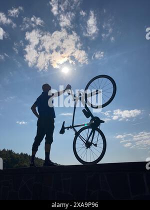 Ein Mann, der ein Fahrrad auf der Schulter trägt und an einer Wand steht Stockfoto