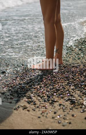 Eine Frau steht auf Felsen am Wasser am Strand Stockfoto