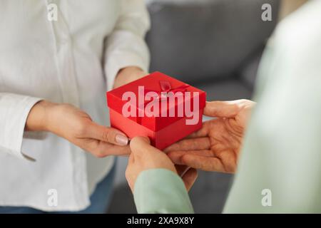 Zwei Personen, männliche und weibliche Hände halten eine Geschenkbox mit rotem Band. Stockfoto