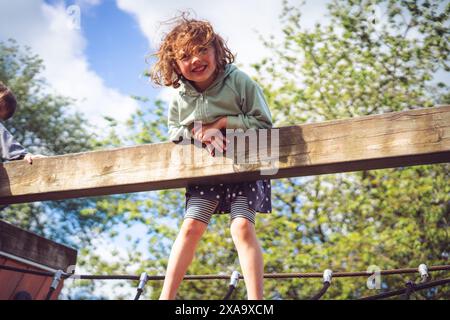 5-jähriges Mädchen, das sich am sonnigen Tag über einen Zaun lehnt Stockfoto