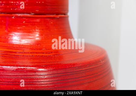 Die runde rote Tonvase steht vor der weißen Wand, Nahaufnahme mit selektivem Weichfokus Stockfoto