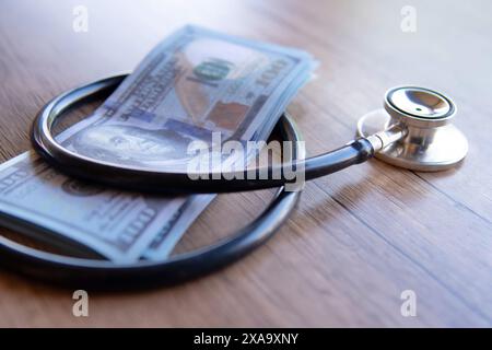 Ein Nahbild eines schwarzen Stethoskops, das um einen Stapel US-Dollar-Scheine gewickelt ist. Kosten der Gesundheitsversorgung, finanzielle Belastung, Kopay-Konzept. Stockfoto