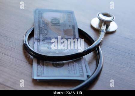 Ein Nahbild eines schwarzen Stethoskops, das um einen Stapel US-Dollar-Scheine gewickelt ist. Kosten der Gesundheitsversorgung, finanzielle Belastung, Kopay-Konzept. Stockfoto