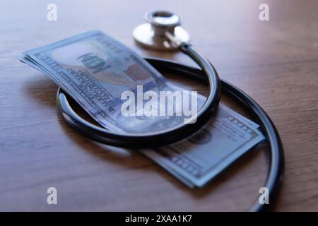 Ein Nahbild eines schwarzen Stethoskops, das um einen Stapel US-Dollar-Scheine gewickelt ist. Kosten der Gesundheitsversorgung, finanzielle Belastung, Kopay-Konzept. Stockfoto