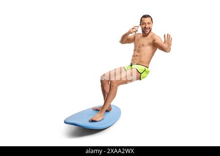 Aufnahme eines Surfers auf einem Board in voller Länge, der die Kamera anlächelt und ein Smartphone auf weißem Hintergrund verwendet Stockfoto