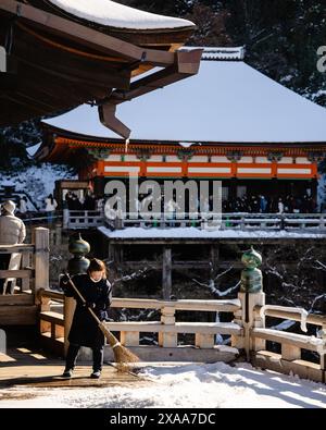 Eine Japanerin, die von einer schneebedeckten Plattform im alten heiligen buddhistischen Tempelkomplex Kiyomizudera in Kyoto, Japan, fegt Stockfoto