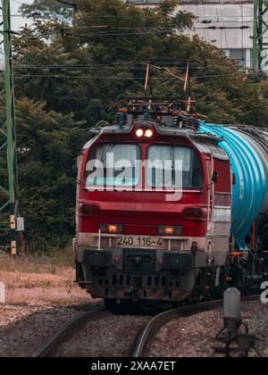 Die rote Lokomotive bewegt sich entlang der gekrümmten Gleise und zieht blaue und grüne Güterwagen. Stockfoto