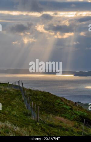 Ein malerischer Blick auf den grünen Hügel und das Meer, das von Sonnenstrahlen beleuchtet wird. Storr, Schottland Stockfoto