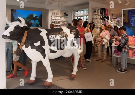 Sitges, Barcelona, Spanien – 05. Juni 2024: Lackiertes Kuhmodell mit Ale-Hop-Logo in einem geschäftigen Geschäft mit verschiedenen Produkten in den Regalen. Stockfoto