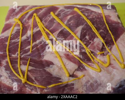 Eine Nahaufnahme von geschnittenem rohem Schweinefleisch mit Senfsauce auf einem Schneidebrett Stockfoto