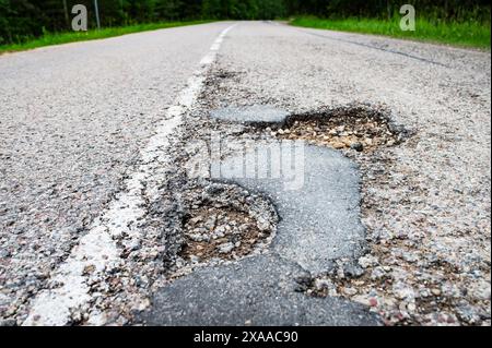 Die Textur von gerissenem altem Asphalt, der reparaturbedürftig ist. Die Straße ist voller Löcher und Schlaglöcher. Litauen 2024 Stockfoto