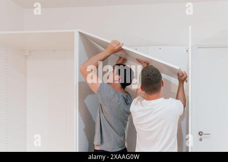 Zwei junge Männer, die in einer neuen Wohnung ein Schrankregal zusammenbauen. Möbelkonzept Stockfoto