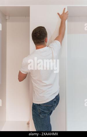 Junger Zimmermann, der zu Hause eine weiße Schranktür zusammenbaut. Möbelkonzept Stockfoto