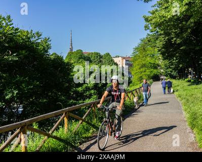 Turin, Italien - 24. Mai 2018: Menschen gehen und ein Mann auf dem Fahrrad entlang des Flusses Dora. Im Hintergrund ist die Mole Antonelliana, das wichtigste Wahrzeichen Stockfoto