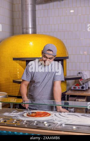 Der Koch gießt Tomatensauce über den gerollten Teig. Chef Hand verteilt pasteurisierte Tomatenpaste auf eine Pizzabasis. der wärmebäcker macht Pizza in der Küche Stockfoto