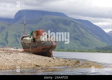 Corpach Shipwreck, Old Boat of Caol, liegt stolz am steinigen Strand von Loch Eil, vor der Kulisse des atemberaubenden Ben Nevis, Schottland Stockfoto