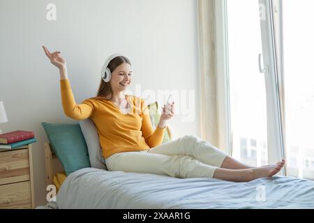 Mädchen, das sich auf dem Bett entspannt und Musik am sonnigen Nachmittag hört Stockfoto