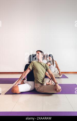 Gruppe von Personen in einem Yoga-Kurs, die paarweise Körperhaltungen machen, während sie im Fitnessstudio auf einer Matte sitzen. Vertikales Format mit Kopierraum. Stockfoto