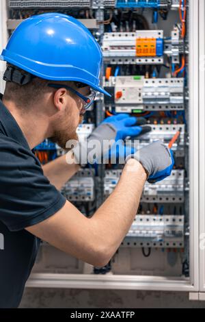 Ein Elektriker arbeitet in einer Schalttafel mit einem elektrischen Anschlusskabel. Stockfoto