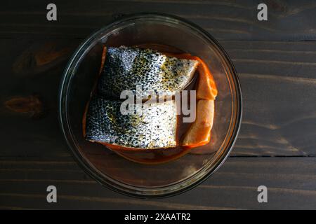 Marinieren von Lachsfilets mit der Hautseite nach oben: Rohe Lachsfilets in einer Glasschale mit der Hautseite nach oben mariniert Stockfoto