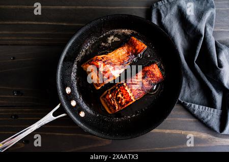 Gebratene Lachsfilet in einer kleinen Antihaft-Skillet: Zwei Lachsfischfilets gebräuntes Olivenöl und Butter in einer Pfanne auf einem dunklen Holztisch Stockfoto