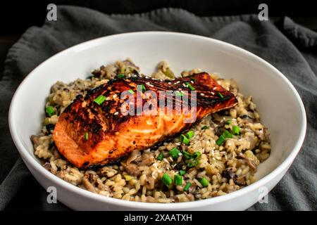 Gebratener Lachs mit Pilz-Risotto in einer Pasta-Schüssel: Mariniertes Lachsfischfilet auf einem Bett aus Pilzrisotto mit Zwiebeln und Sesamgarnitur Stockfoto