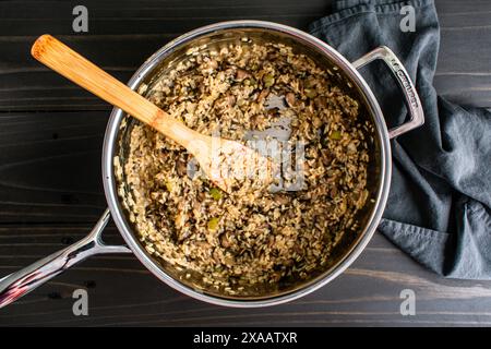 Pilz-Risotto in einer großen Sautepfanne mit Holzspachtel: Frisch gekochtes Risotto in einer Edelstahlpfanne, gerührt mit einem Bambusspachtel Stockfoto