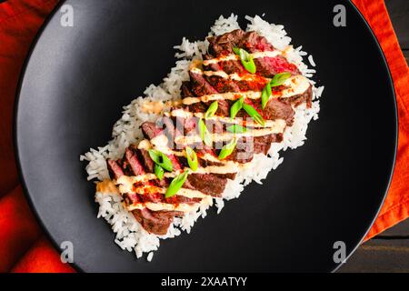 Koreanisches Rock Steak mit Kimchi Aioli über Jasminreis: Gegrilltes Rock Steak in Scheiben geschnitten und garniert mit Aioli, Gochugaru, Zwiebeln und Sesamsamen Stockfoto