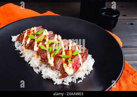 Koreanisches Rock Steak mit Kimchi Aioli über Jasminreis: Gegrilltes Rock Steak in Scheiben geschnitten und garniert mit Aioli, Gochugaru, Zwiebeln und Sesamsamen Stockfoto