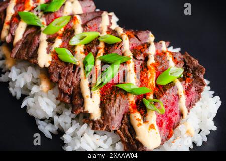 Koreanisches Rock Steak mit Kimchi Aioli über Jasminreis: Gegrilltes Rock Steak in Scheiben geschnitten und garniert mit Aioli, Gochugaru, Zwiebeln und Sesamsamen Stockfoto