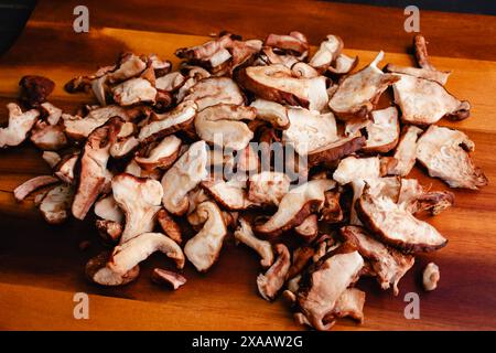 Geschnittene und zerrissene Shiitake-Pilze Nahaufnahme auf einem Schneidebrett: Frische Shitake-Pilze, die in mundgroße Stücke gerissen wurden, auf einem Holzhintergrund aufgehäuft Stockfoto