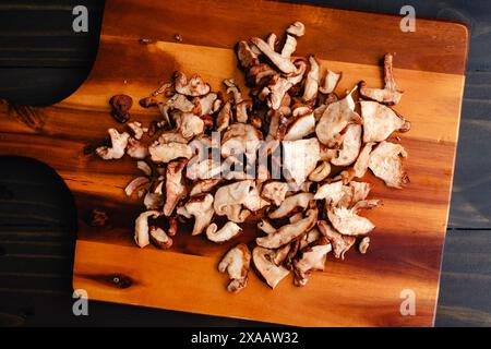 Haufen geschnittener und zerrissener Shiitake-Pilze auf einem Schneidebrett: Frische Shitake-Pilze, die in mundgroße Stücke gerissen werden, auf einem hölzernen Hintergrund Stockfoto