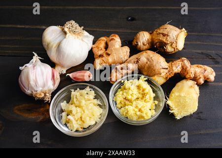 Geriebener Ingwer und Knoblauch in Mise Schalen: Bereiten Sie Schüsseln mit geriebener Knoblauchzehen und Ingwerwurzel auf einem Holztisch vor Stockfoto