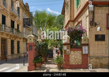 Sitges, Barcelona, Spanien - 03. Juni 2024: Königlicher Eingang zum Sitges Hotel, geschmückt mit leuchtenden rosafarbenen Säulen und üppigem Laub, vor einem ruhigen Blau Stockfoto