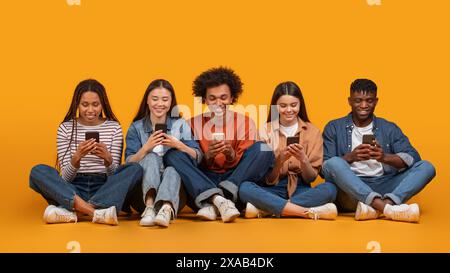Internationale Gruppe von Freunden, die Smartphones verwenden, während sie auf Gelb sitzen Stockfoto