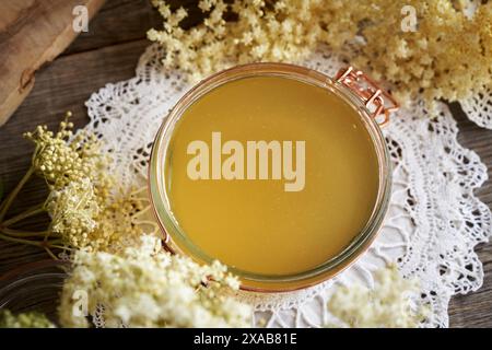 Ein Glas hausgemachter Holunderblütensirup mit frischen Sambucus nigra-Blüten auf einem Tisch Stockfoto